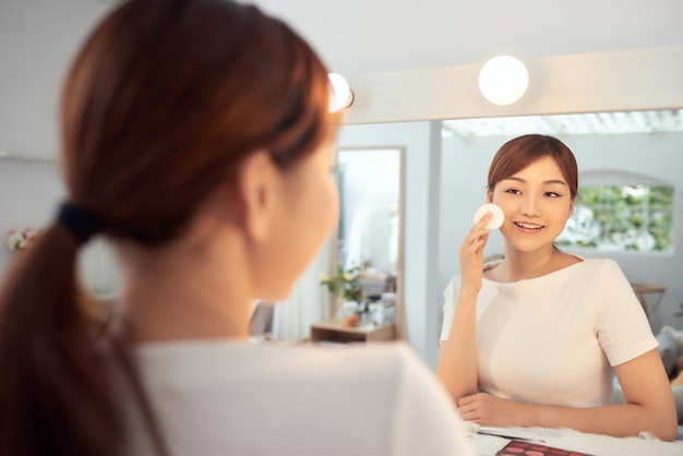 Jeune femme asiatique nettoyant son visage devant le miroir