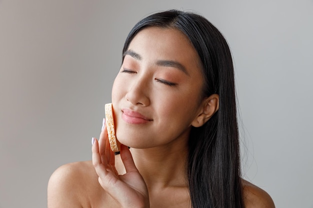 Jeune femme asiatique nettoyant le visage avec une éponge cosmétique