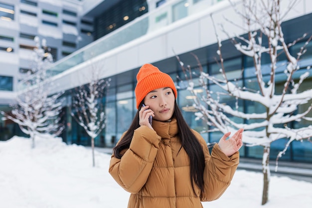 Jeune femme asiatique parlant au téléphone marchant un jour d'hiver enneigé un étudiant sur le campus