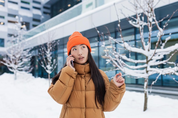 Jeune femme asiatique parlant au téléphone marchant un jour d'hiver enneigé un étudiant sur le campus