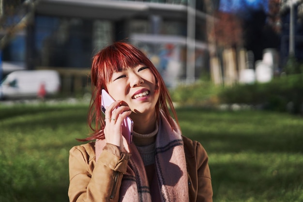 Une jeune femme asiatique passe un appel téléphonique en parlant sur un smartphone mobile et en marchant dans la rue