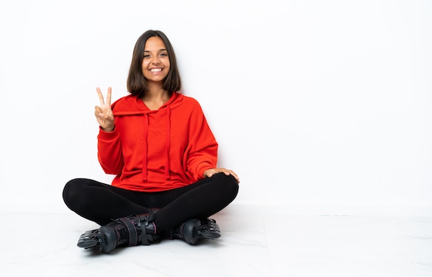 Jeune femme asiatique avec des patins à roulettes sur le sol souriant et montrant le signe de la victoire