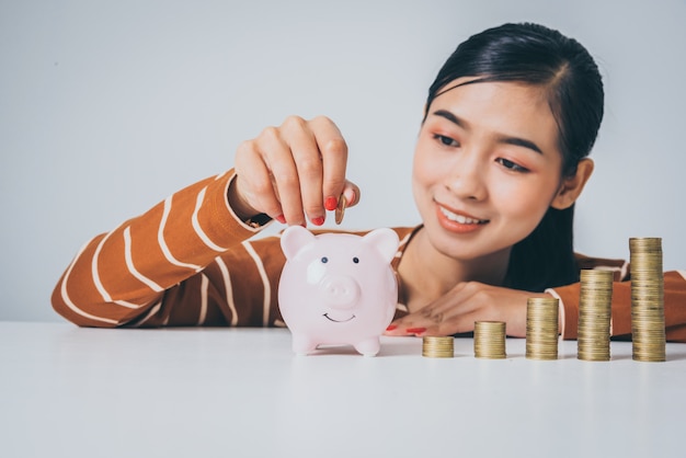 Jeune femme asiatique avec pile de pièces et tirelire