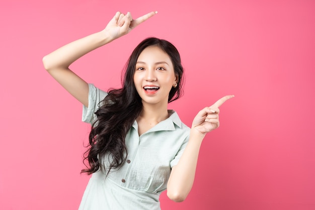 Jeune femme asiatique pointant vers le haut avec un visage joyeux sur rose