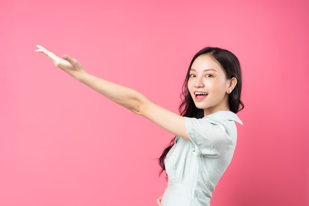 Jeune femme asiatique pointant vers le haut avec un visage joyeux sur rose