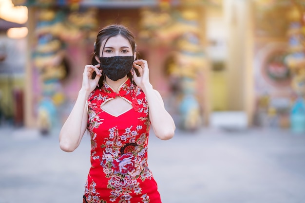 Jeune femme asiatique portant un cheongsam chinois traditionnel rouge, et porte un masque de protection