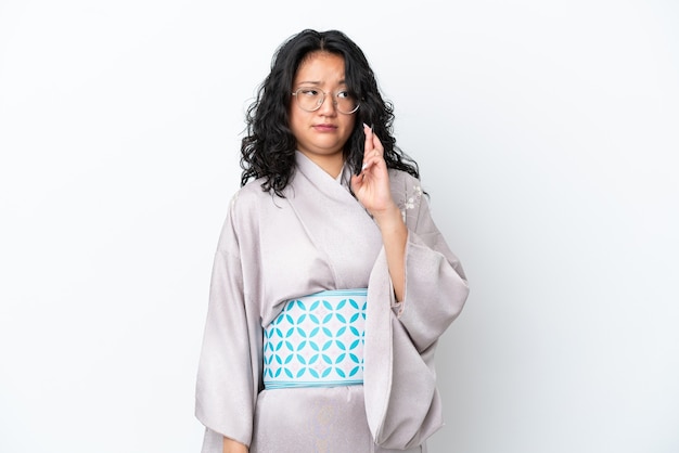 Jeune femme asiatique portant un kimono isolé sur fond blanc avec les doigts croisés et souhaitant le meilleur