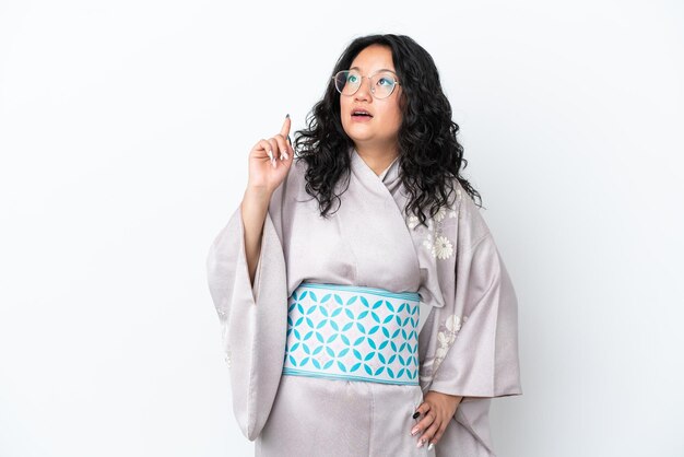 Jeune femme asiatique portant un kimono isolé sur fond blanc pensant à une idée pointant le doigt vers le haut