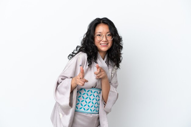 Jeune femme asiatique portant un kimono isolé sur fond blanc pointant vers l'avant et souriant