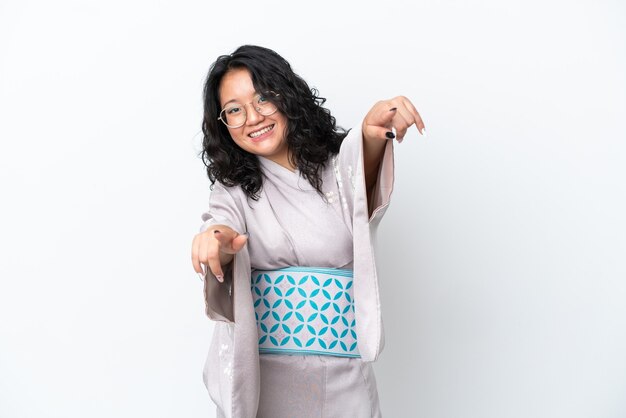 Jeune femme asiatique portant un kimono isolé sur fond blanc pointe le doigt vers vous tout en souriant