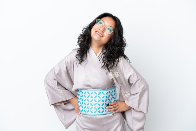 Jeune femme asiatique portant un kimono isolé sur fond blanc posant avec les bras à la hanche et souriant