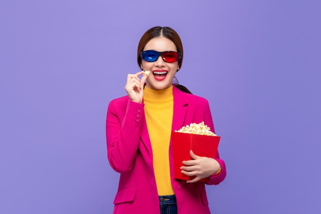 Jeune femme asiatique portant des lunettes 3D appréciant manger du pop-corn et regarder un film