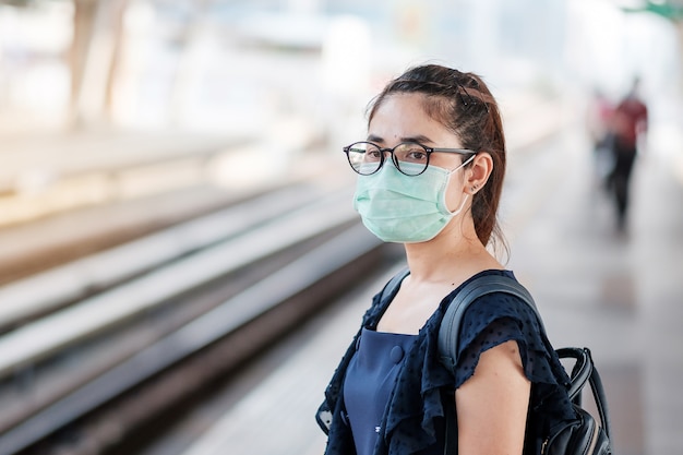 Jeune femme asiatique portant un masque facial chirurgical contre un nouveau coronavirus ou maladie à virus Corona (Covid-19) à la gare publique.