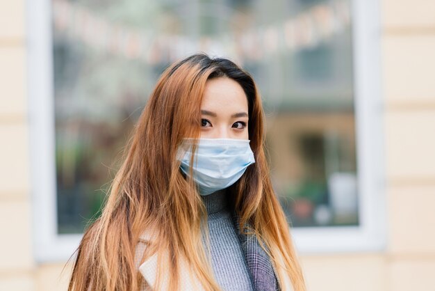 Une jeune femme asiatique portant un masque facial se tient dans une rue domestique. Nouvelle épidémie normale de covid-19