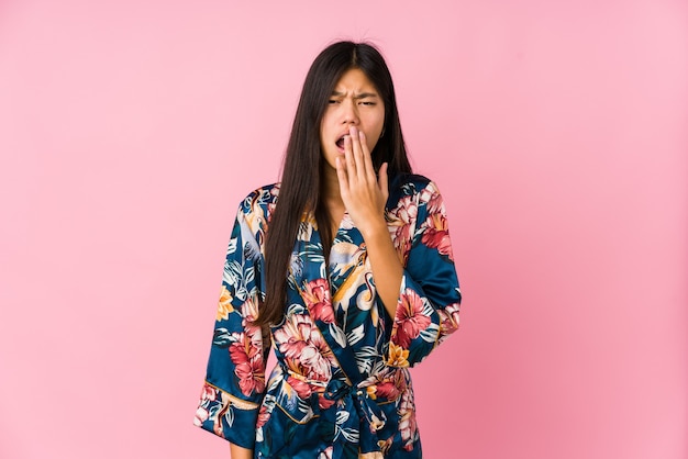 Jeune femme asiatique portant un pyjama kimono bâillant montrant un geste fatigué couvrant la bouche avec la main.