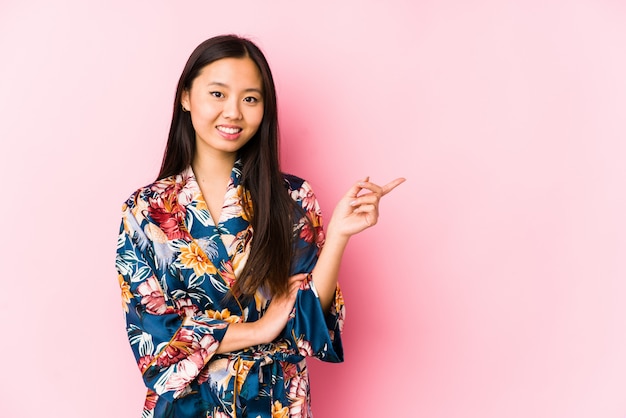 Jeune femme asiatique portant un pyjama kimono souriant pointant gaiement avec l'index loin