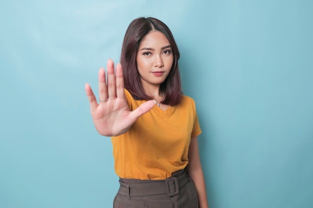 Jeune femme asiatique portant un t-shirt décontracté sur fond bleu isolé faisant un panneau d'arrêt avec la paume de la main