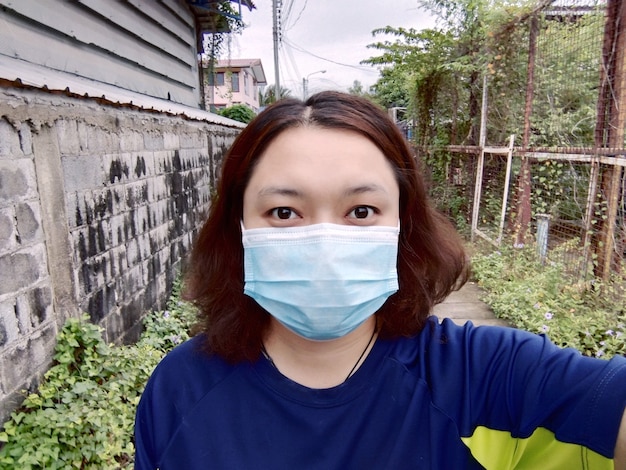 Une jeune femme asiatique porte un masque pour la prévention et la protection Covid-19 qui se propagent beaucoup en Thaïlande. Elle Selfie avec un smartphone pendant la quarantaine et travaille à domicile. Nouvelle normalité pour le confinement.