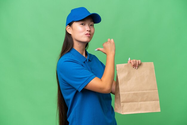 Jeune femme asiatique prenant un sac de plats à emporter sur fond isolé fier et satisfait