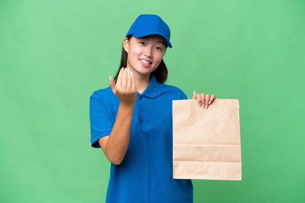 Jeune femme asiatique prenant un sac de plats à emporter sur fond isolé invitant à venir avec la main Heureux que vous soyez venu