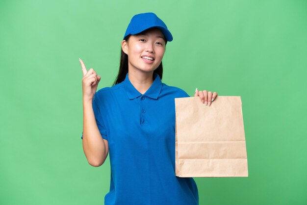 Jeune femme asiatique prenant un sac de plats à emporter sur fond isolé montrant et levant un doigt en signe du meilleur