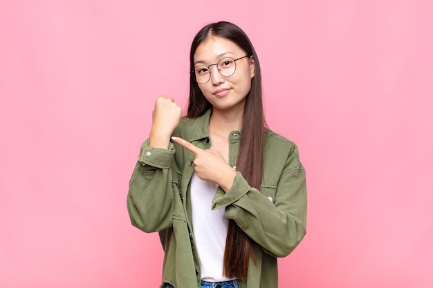 Jeune femme asiatique à la recherche d'impatience et en colère, pointant sur montre, demandant la ponctualité