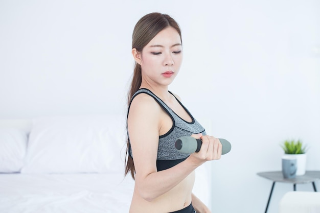 Photo jeune femme asiatique de remise en forme faisant des exercices avec des haltères d'entraînement dans la formation de remise en forme de la chambre et le concept de style de vie