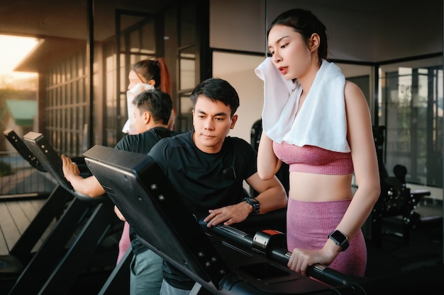 Jeune femme asiatique de remise en forme mince avec une serviette près d'un entraîneur personnel l'aider à s'entraîner sur le tapis roulant dans la salle de gym L'athlète mène un mode de vie sain Entraînement cardio pour perdre du poids