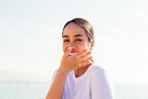 Jeune femme asiatique riant et couvrant sa bouche avec sa main, concept de bonheur et de pureté