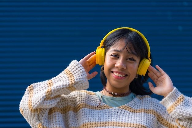 Jeune femme asiatique s'amusant à écouter de la musique avec un casque jaune sur fond bleu universitaire