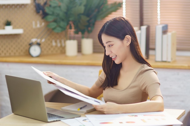 Photo jeune femme asiatique s'asseoir dans le salon à l'aide d'un ordinateur portable et étudier à partir du graphique du tableau financier pour l'investissement femme d'affaires chinoise apprenant et travaillant en ligne pour démarrer une petite entreprise au bureau à domicile