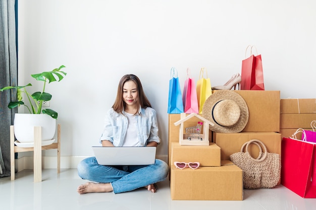 Jeune femme asiatique avec sac à provisions coloré, articles de mode et pile de boîtes en carton à la maison, concept de magasinage en ligne de site Web avec espace de copie