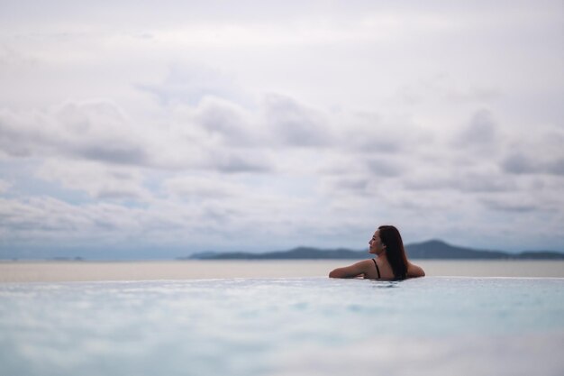 Photo une jeune femme asiatique se détend dans une piscine à infini en train de regarder une belle personne avec vue sur la mer