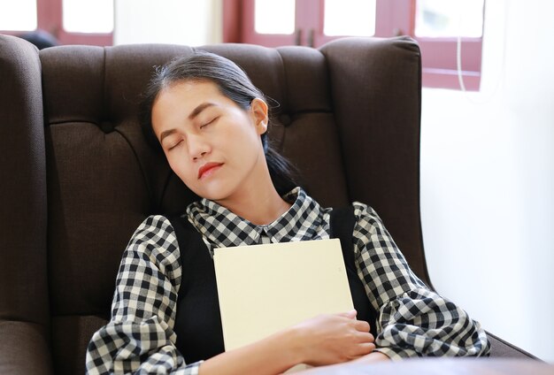 Jeune femme asiatique se détendre et dormir sur le canapé dans la bibliothèque