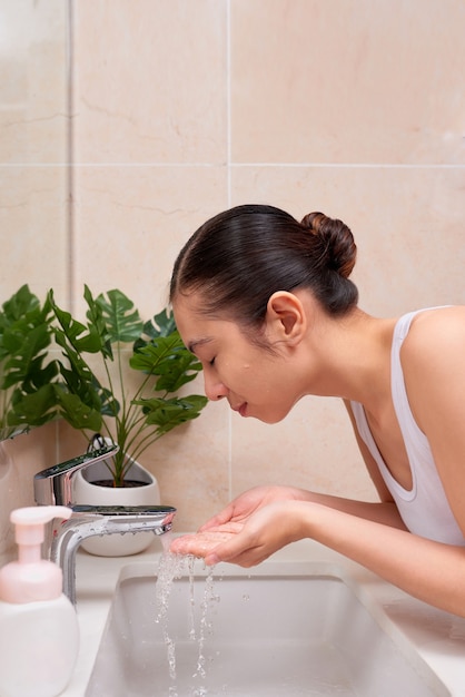 Jeune femme asiatique se lavant le visage sur l'évier