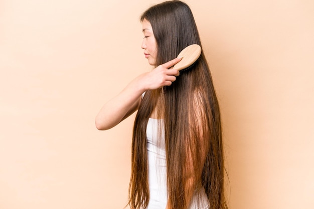 Jeune femme asiatique se peignant les cheveux isolé sur fond beige