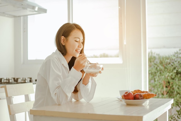 Jeune femme asiatique se réveille rafraîchie le matin et se détend en mangeant du café, des cornflakes, du pain et des pommes pour le petit-déjeuner à la maison en vacances. Asiatique, asie, détente, petit-déjeuner, rafraîchissement, concept de style de vie.