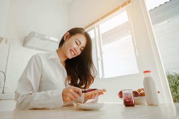 Jeune femme asiatique se réveille rafraîchie le matin et se détend en mangeant du café, des cornflakes, du pain et des pommes pour le petit-déjeuner à la maison en vacances. Asiatique, asie, détente, petit-déjeuner, rafraîchissement, concept de style de vie.