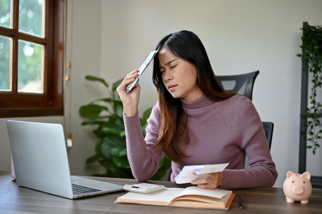 Une jeune femme asiatique se sent contrariée et stressée après avoir regardé les factures.