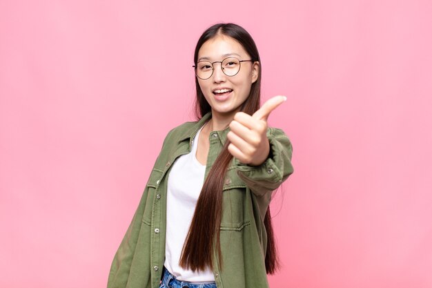 Jeune femme asiatique se sentir fière, insouciante, confiante et heureuse, souriant positivement avec les pouces vers le haut