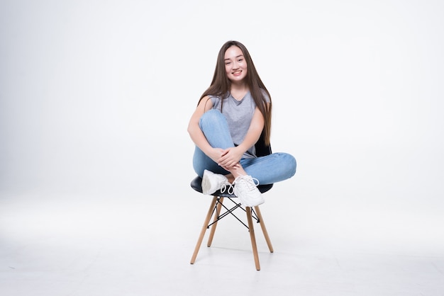 Jeune femme asiatique séduisante assise sur la chaise isolée sur un mur blanc