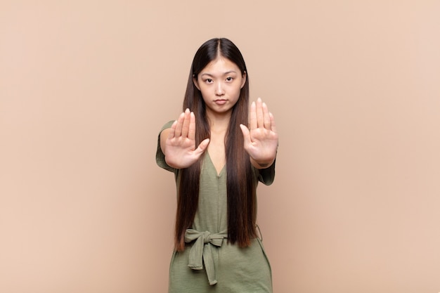 Jeune femme asiatique à la sérieuse, malheureuse, en colère et mécontente d'interdire l'entrée ou de dire arrêter avec les deux paumes ouvertes