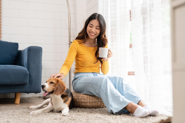 Jeune femme asiatique avec son chien beagle se détendre et boire du café assis dans le salon à la maison