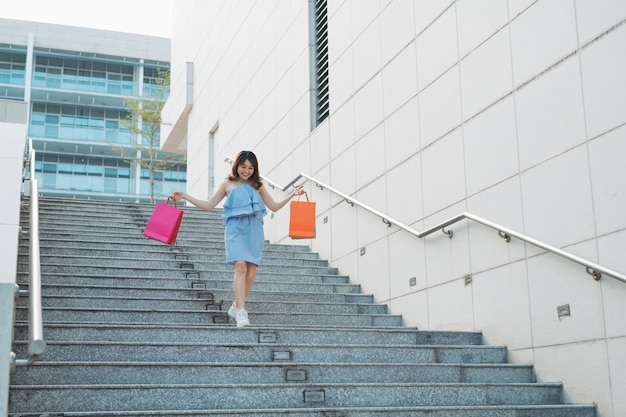 Une jeune femme asiatique souriante aime faire du shopping avec un sac coloré en descendant les escaliers.