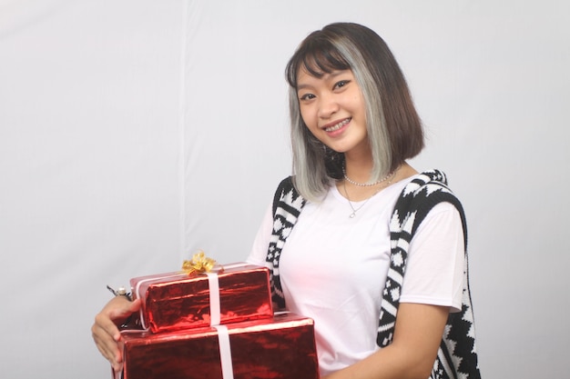 Une jeune femme asiatique souriante apporte des coffrets cadeaux fond blanc.