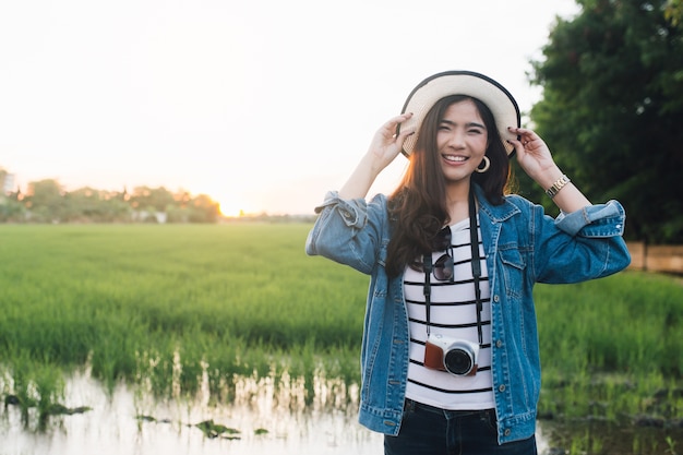 Jeune femme asiatique souriante au chapeau avec caméra. Fille profitant de la belle nature avec sunse