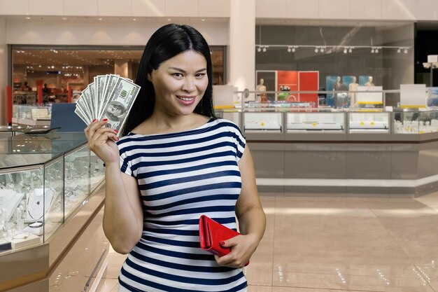 Une jeune femme asiatique souriante montre un fan de dollars du portefeuille rouge