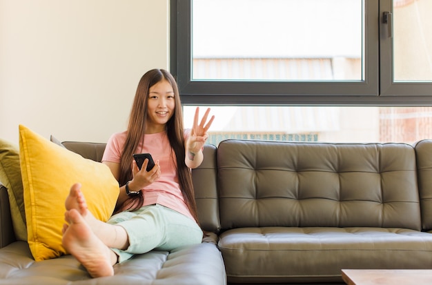 Jeune femme asiatique souriante et à la recherche amicale, montrant le numéro trois ou troisième avec la main en avant, compte à rebours