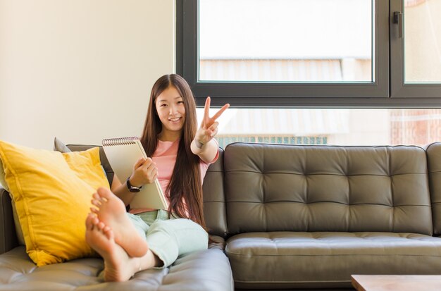 Jeune femme asiatique souriante et à la recherche heureuse, insouciante et positive, gesticulant la victoire ou la paix d'une main