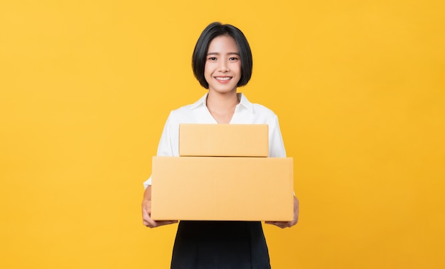 Jeune femme asiatique souriante tenant des boîtes sur fond orange clair